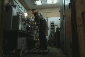 Man in Gray Jacket Standing in Front of Gray Metal Machine