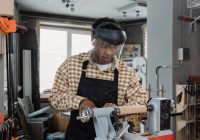 Man Wearing Checkered Long Sleeves and an Apron in a Workshop working on a lathe