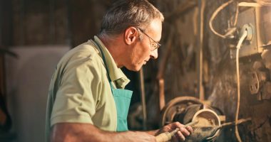 A senior craftsman focuses intently while working with tools in a dimly lit workshop.